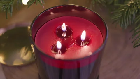 Red scented candle burning by Christmas tree with warm festive lights, 4K Stock Footage 324595063