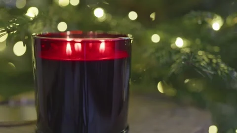 Red scented candle burning by Christmas tree with warm festive lights, 4K Stock Footage 324595069