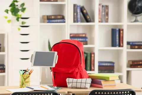 Red school backpack with digital tablet and books on wooden desk in modern cl Stock Photos