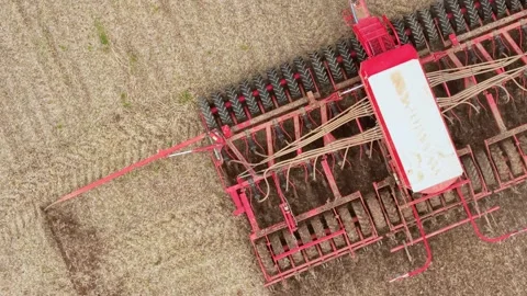 Red seeding implement with multiple wheels and seed delivery tubes across Stock Footage 345501194