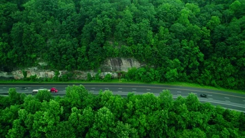 Red semi truck with flatbed trailer drives along forest highway past rocky Stock Footage 311426769