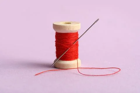Red sewing thread with needle on lilac background Stock Photos