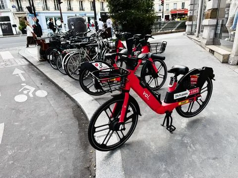 Red shared bicycles parked on a Paris, France sidewalk beside a bike lane f.. Stock Photos