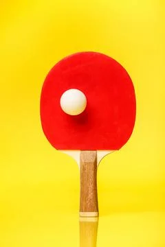 Red side of a ping pong racket with a white ball standing on a yellow backg.. Stock Photos