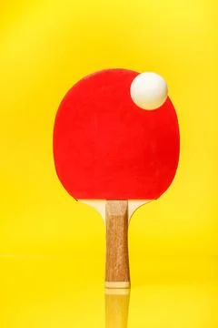 Red side of a ping pong racket with a white ball standing on a yellow backg.. Stock Photos