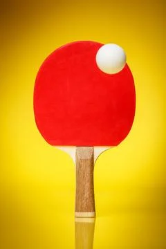 Red side of a ping pong racket with a white ball standing on a yellow backg.. Stock Photos