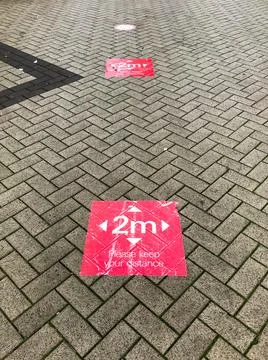 Red signs on a patterned pavement ask people to 'keep your distance' with 2m Stock Photos