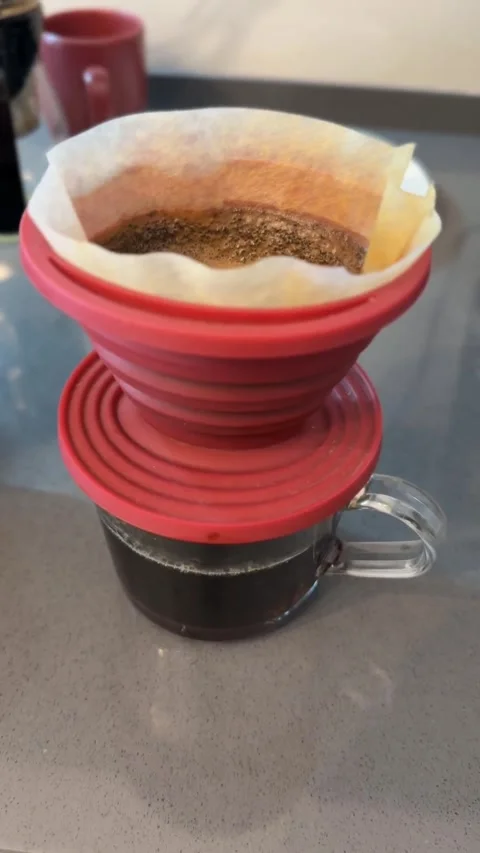 A red silicone coffee dripper brewing coffee over a glass cup on a kitchen .. Vídeo Stock 331031093
