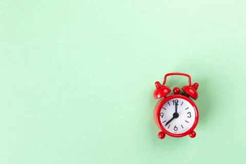 Red small alarm clock on light pastel green background with copy space, flat Stock Photos