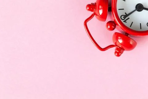 Red small alarm clock on light pastel pink background with copy space, flat l Stock Photos