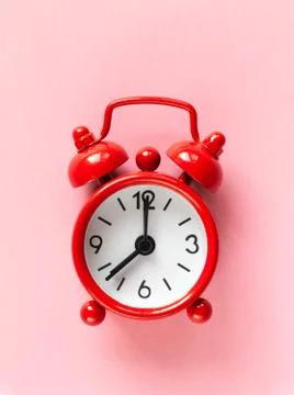 Red small alarm clock on light pastel pink background, flat lay, macro. Minim Stock Photos