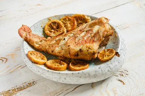 Red snapper served with roasted lemon slices on a white plate on a wooden tab Stock Photos