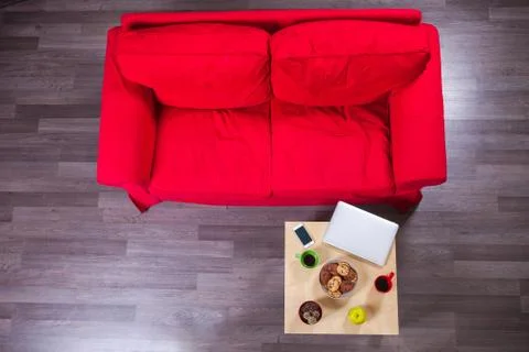 Red sofa and table with laptop, cellphone, cups of coffee and cookies Stock Photos
