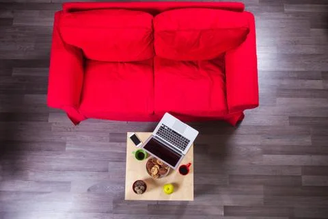 Red sofa and table with laptop, cellphone, cups of coffee and cookies. Stock Photos