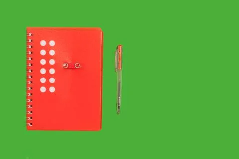 Red spiral notebook on a green surface Stock Photos