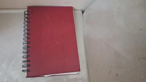 Red spiral notebook resting on a flat white textured tabletop surface Stock Photos