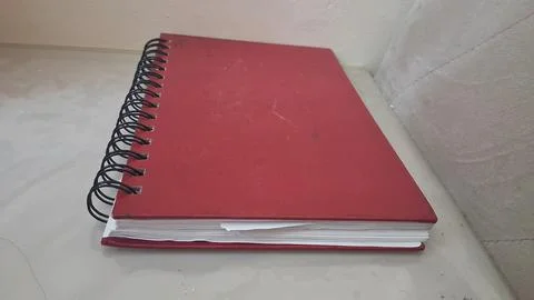 Red spiral notebook rests on a smooth light colored floor surface Stock Photos