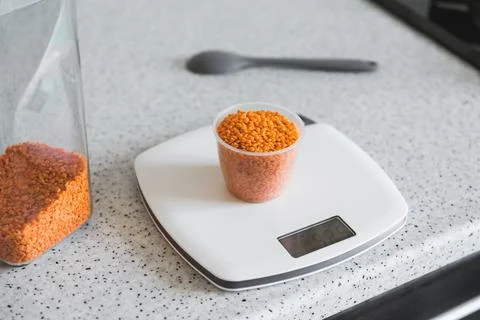 Red split lentils in a measuring cup on white digital scale displaying Stock Photos