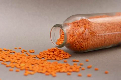 Red split lentils scattered on a grey background from glass jar Stock Photos