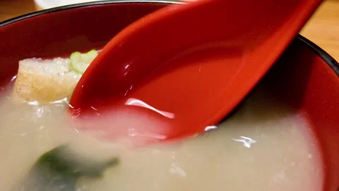 Red spoon in a steaming bowl of miso soup with tofu and green onions Video stock 321670053