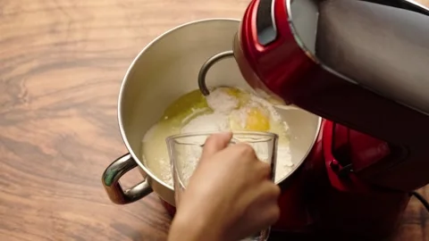 Red stand mixer, adding eggs with a glass measuring cup Stock Footage 281459896