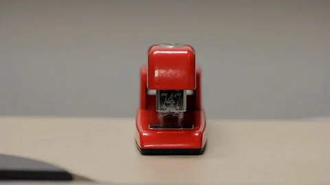 Red stapler being used to staple pages in an office Stock Footage 92525366