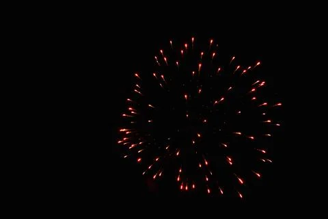 Red starry sphere firework explodes in the dark of night sky Stock Photos