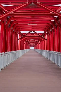 Red steel structure forms a symmetrical bridge with a long wooden walkway, Fotos de archivo
