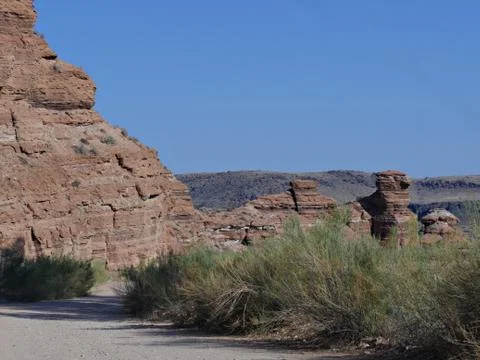 Red steep cliffs and thick shrubbery border a rugged road toward a ghost town Stock Photos