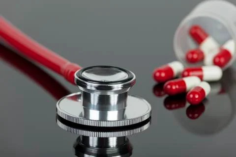 Red stethoscope on lab worktop with spilled pill capsules Stock-Fotos