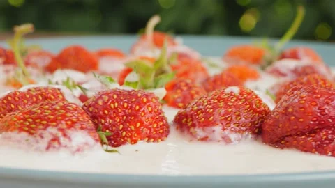 Red strawberries float in heavy cream on a green background rotation in a circle 库存影片 202601071