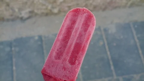 Red strawberry flavored Popsicle on a background of asphalt, concrete Stock Footage 91023235