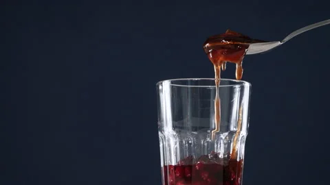 Red strawberry jam falls on a spoon, below a glass of cranberry and ice cocktail Stock Footage 178479863