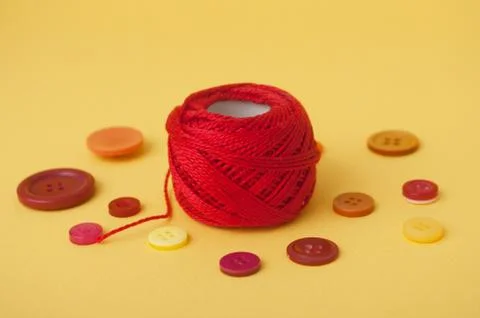 Red string bobbin and plastic buttons on yellow background Foto stock