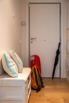 A red suitcase, backpack, and umbrella wait by the front door. Stock Photos