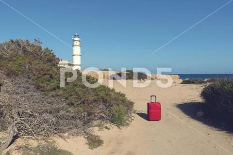 Red suitcase on a path to lighthouse at Cap de ses Salines. Selective focus Stock Photos