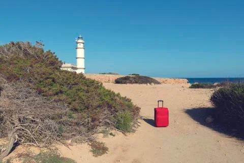 Red suitcase on a path to lighthouse at Cap de ses Salines. Selective focus Stock Photos