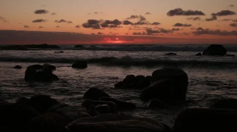 Red sun setting above ocean with rocks Stock Footage 59771193