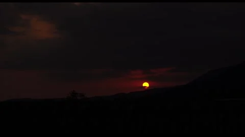 Red Sun Setting Behind Dark Mountain Silhouette at Dusk Stock Footage 343455160