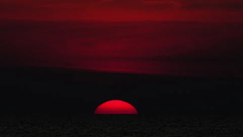 Red sun setting below ocean horizon under dramatic sky Video stock 337158721