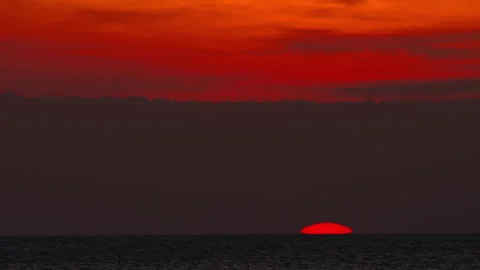 Red sun setting over ocean horizon under dramatic sky Stock Footage 338354008