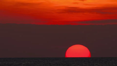 Red sun setting over sea horizon under dramatic orange sky Stock Footage 338129215