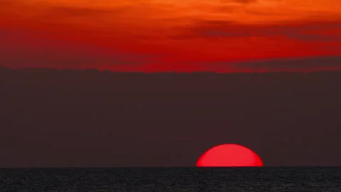 Red sun setting over sea horizon under dramatic orange sky Stockbeeldmateriaal 341695978