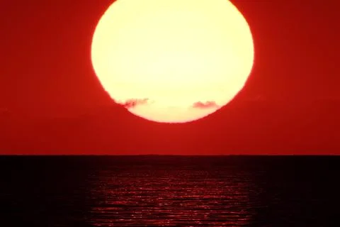 Red sun setting over the sea water with horizon under evening sky Stock Photos