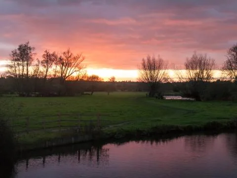 Red sun setting sky dramatic autumn over empty open green countryside night d Stock Photos