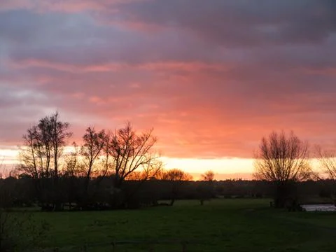 Red sun setting sky dramatic autumn over empty open green countryside night d Stock Photos