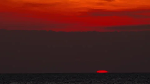 Red sun sinking below ocean horizon under dramatic sky Stock Footage 339205656