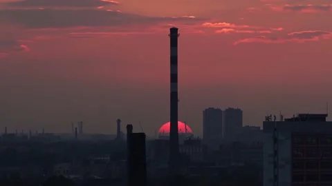 Red sun sinks below the horizon against the backdrop of the city's industrial Stock Footage 141364055
