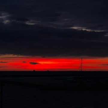 Red sunset against black clouds with steam on horizon Stock Photos