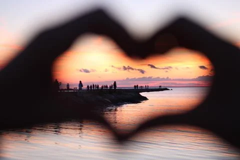 Red sunset behind two arms showing heart Stock Photos